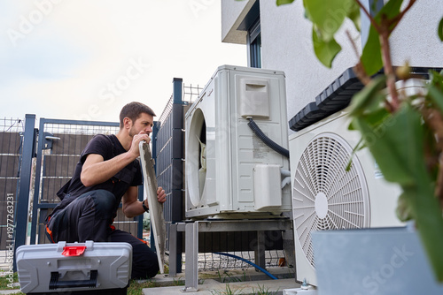 Obraz na płótnie Technician servicing outdoor heat pump unit with removed panel near residential building