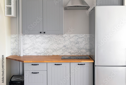 Empty modern minimal tiny grey color kitchen, marble wall, solid natural wood butcher block countertop with built in small stove, black handles.