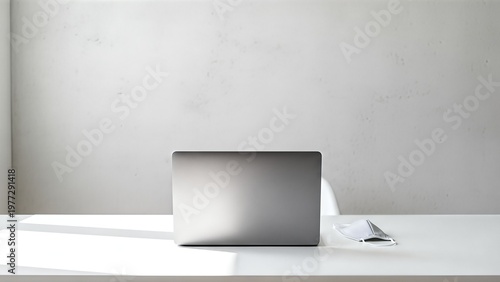 A closed silver laptop computer sits on a white desk with a minimalist background and soft natural light.