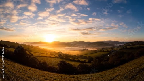 Hilly landscape bathed in golden sunrise, with a misty valley below