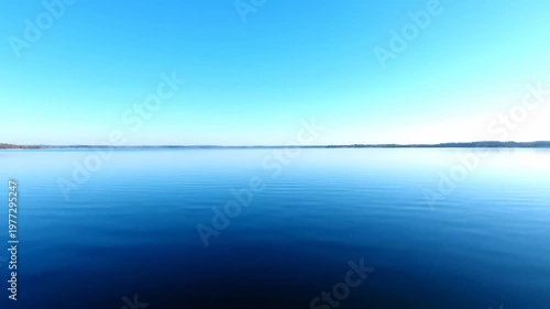 Horizon over serene lake under clear blue sky. Water rippling slightly