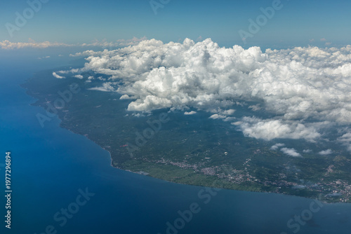 Wide aerial coastline of Bali with cloud formation and visible settlements from airplane.