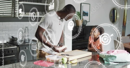 Father preparing sandwich, packing lunch for school while daughter watching, icons overlaying frame