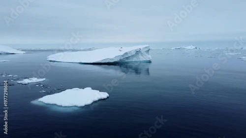 Icebergs float in a vast ocean under a cloudy sky, serene and vast