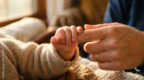 Tender close-up of a tiny baby hand holding a mother's finger with a gold wedding band in warm sunlight, maternal love concept