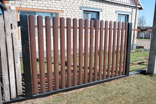 Modern brown metal euro fence panels home garden w section palisade picket with vertical slats and black posts. New privacy fencing, showcasing property boundary and residential security.