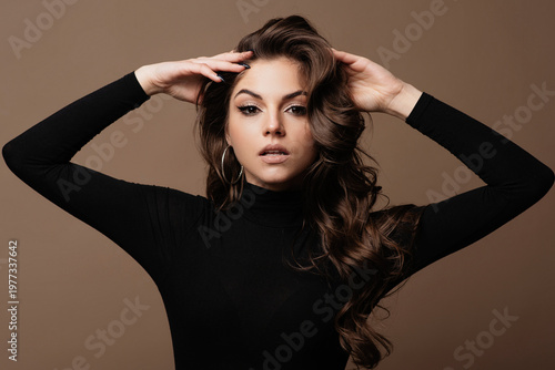Elegant young woman with voluminous wavy hair and striking makeup posing confidently
