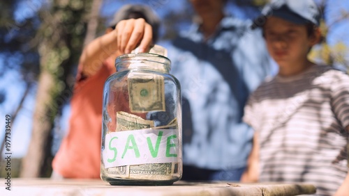 Bild auf Leinwand Child's hand dropping dollar bills into a transparent glass jar labeled save, te