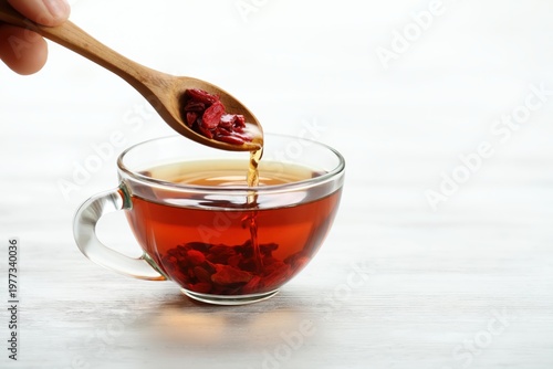 Goji berries cascade from a wooden spoon into a warm cup of herbal tea for wellness