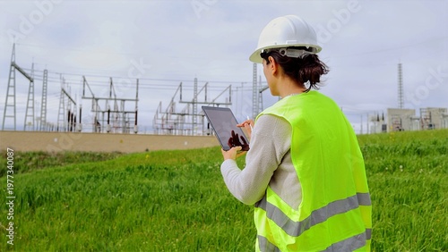 Female engineer observing a power station at a renewable energy facility, utilizing a tablet to manage grid operations and ensuring the sustainability of critical infrastructure