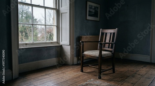 Old wooden chair sits by a large window in a dimly lit room with a picture