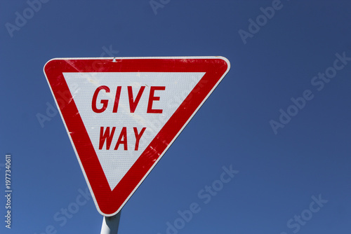 Foto Closeup of a GIVE WAY road sign isolated against a blue sky commonly known in some regions as a yield sign