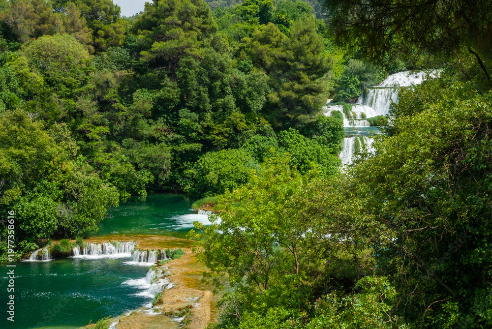 Fototapeta premium Stunning series of cascading waterfalls flowing through lush green forest with turquoise pools and mineral-rich terraces, creating vibrant, untouched natural paradise. Krka National Park is in Croatia
