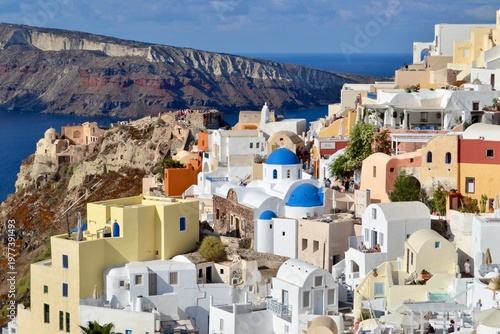 Oia, a picturesque village in Santorini, Greece, features iconic Cycladic architecture with white-washed buildings and blue domed roofs. Positioned on a cliff overlooking the caldera
