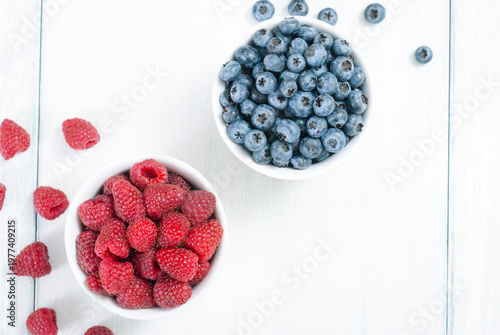 bilberry and raspberry fruits at white ceramic cup, on bright wood table