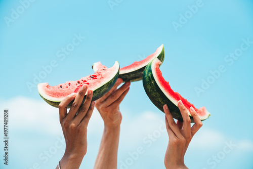 Photos Hands raising fresh watermelon slices against bright blue sky summer refreshment