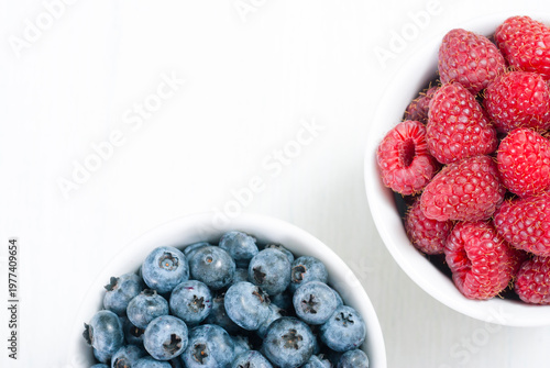 bilberry and raspberry fruits at white ceramic cup, on bright wood table
