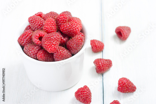 raspberry fruits at white ceramic cup, on bright wood table