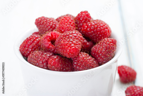 raspberry fruits at white ceramic cup, on bright wood table