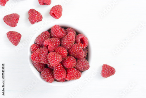 raspberry fruits at white ceramic cup, on bright wood table