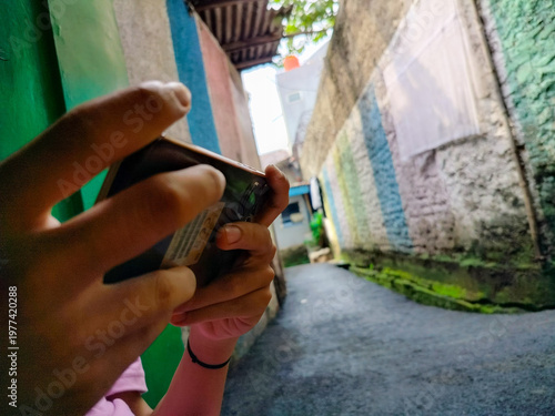 Close-up of a person holding and typing on a smartphone outdoors with a narrow alley background. Concept of mobile communication, social media browsing, and digital connection in urban environment.