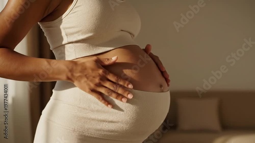 Close up of a pregnant woman gently stroking her belly in warm natural sunlight at home