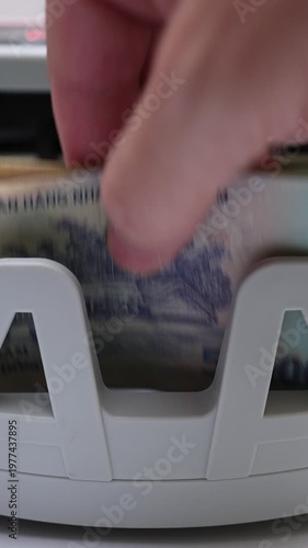 Macro shot of banknote counting machine with Vietnamese Dong money (VND). Automatic currency counter equipment processing paper bill with village landscape vignette. Finance industry in Vietnam.