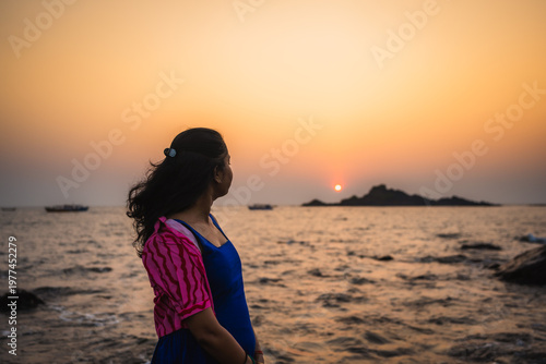 Silhouette of a woman standing by the sea during sunset with waves and rocky shoreline