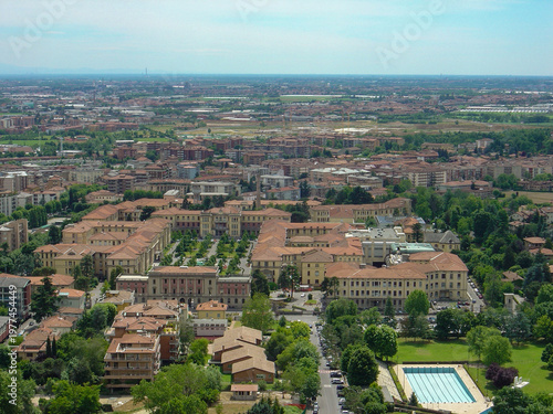 Aerial view of Bergamo with the historic hospital complex in the foreground, surrounded by residential buildings, greenery, and a calm urban landscape under soft daylight.