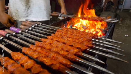 Tableau sur toile Kebabs grilling live on skewers over open fire, showcasing smoky flavor, flames,