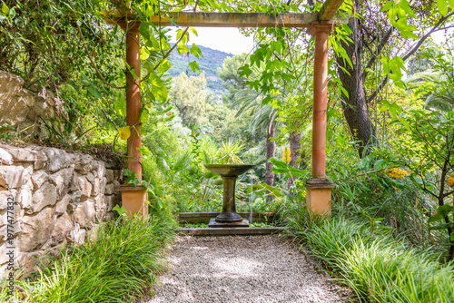 Gazebo perspective with fountain in romantic garden. Green idyllic landscaped patio.