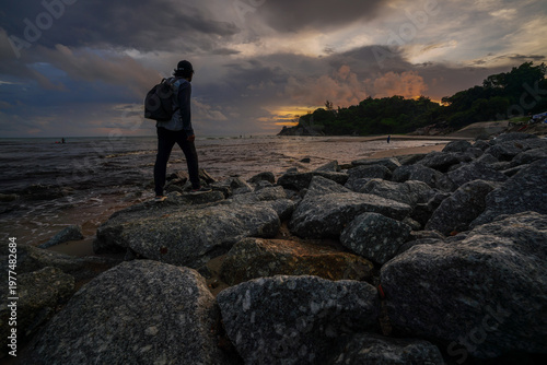 A lone traveler standing on rocky shores at dusk.