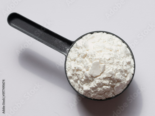 A black measuring spoon filled with white powder on a plain surface