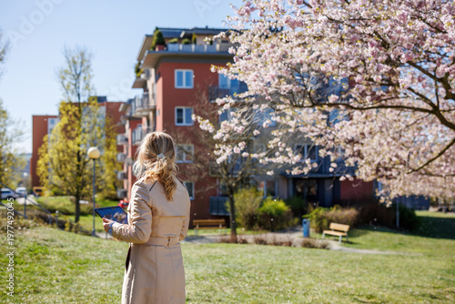 Property consultant analyzing housing options with tablet in modern neighborhood. Woman real estate agent in residential district area