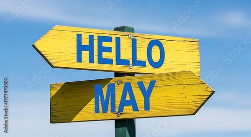 Hello May greeting on yellow wooden directional sign, spring season welcome message on rustic signpost, bright yellow arrow signs against blue sky