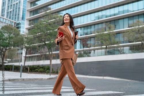Obraz na płótnie Asian businesswoman using smartphone on city street, professional career woman checking online banking and finance apps, walking near business office buildings in urban downtown