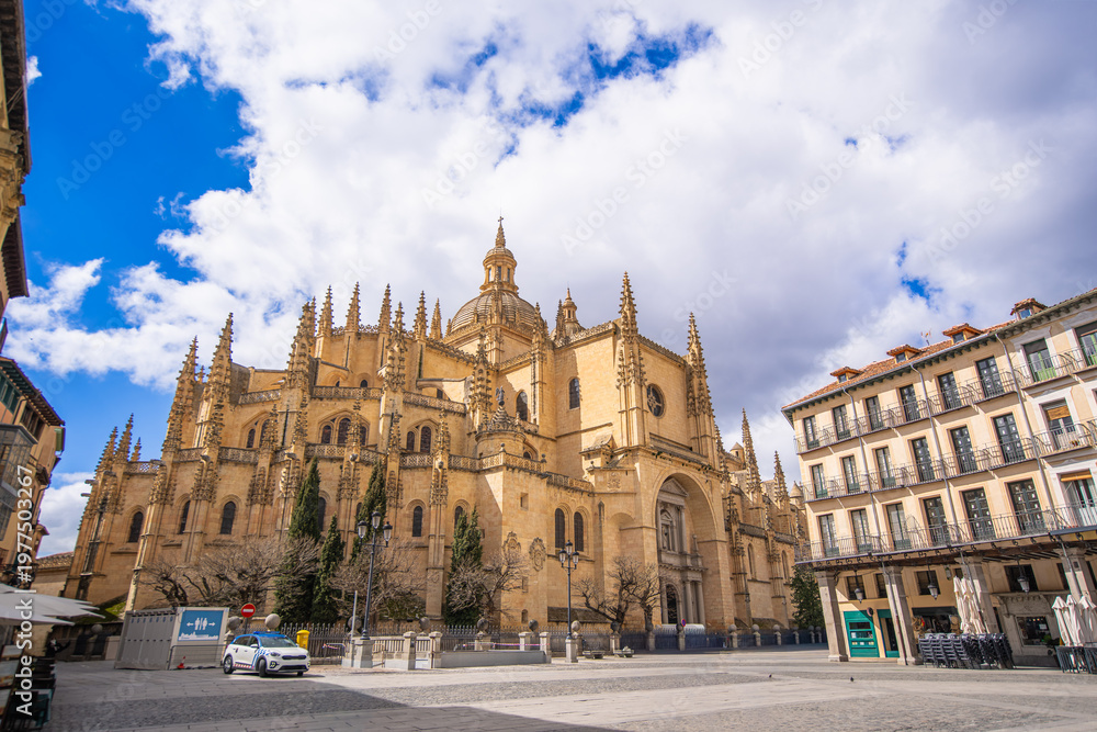 Obraz premium The magnificent Segovia Cathedral, Spain's last Gothic cathedral, stands proudly in the historic Plaza Mayor. Its intricate spires and detailed facade are visible under a blue sky with white clouds.