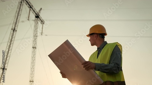 Energy auditor consulting blueprints during transmission tower inspection