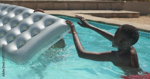 African American dad and son, youth swimming toward dad, pushing and steadying home pool mattress