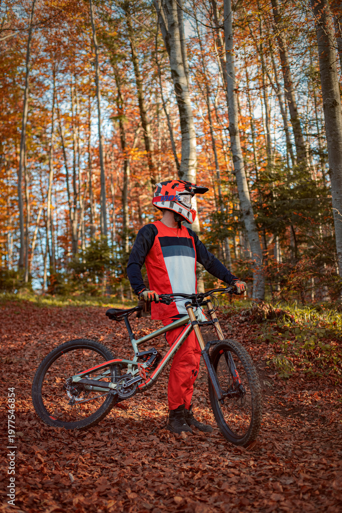 Naklejka premium Mountain biker standing with trail bike in autumn forest