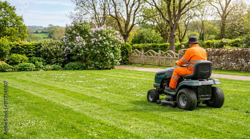 Professional gardener mowing green lawn with riding mower in landscaped garden. Spring lawn care, landscaping maintenance and outdoor property service concept.