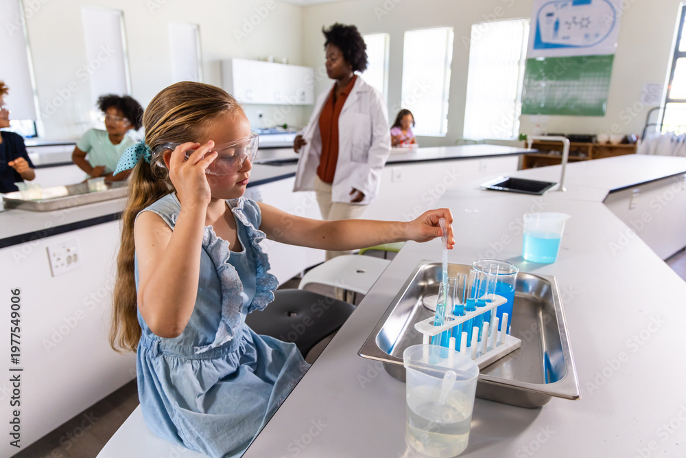 Naklejka premium Diverse teacher and class watching child wearing goggles handling pipette and test tubes at lab