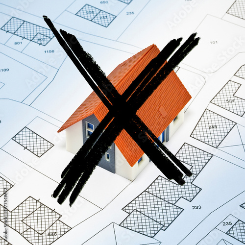 HOUSE MODEL CROSSED OUT ON PLANS SYMBOLIZING UNAFFORDABLE HOUSING, RISING PROPERTY PRICES, INABILITY TO BUY, REAL ESTATE CRISIS, FINANCIAL STRESS, AND HOUSING PROBLEMS