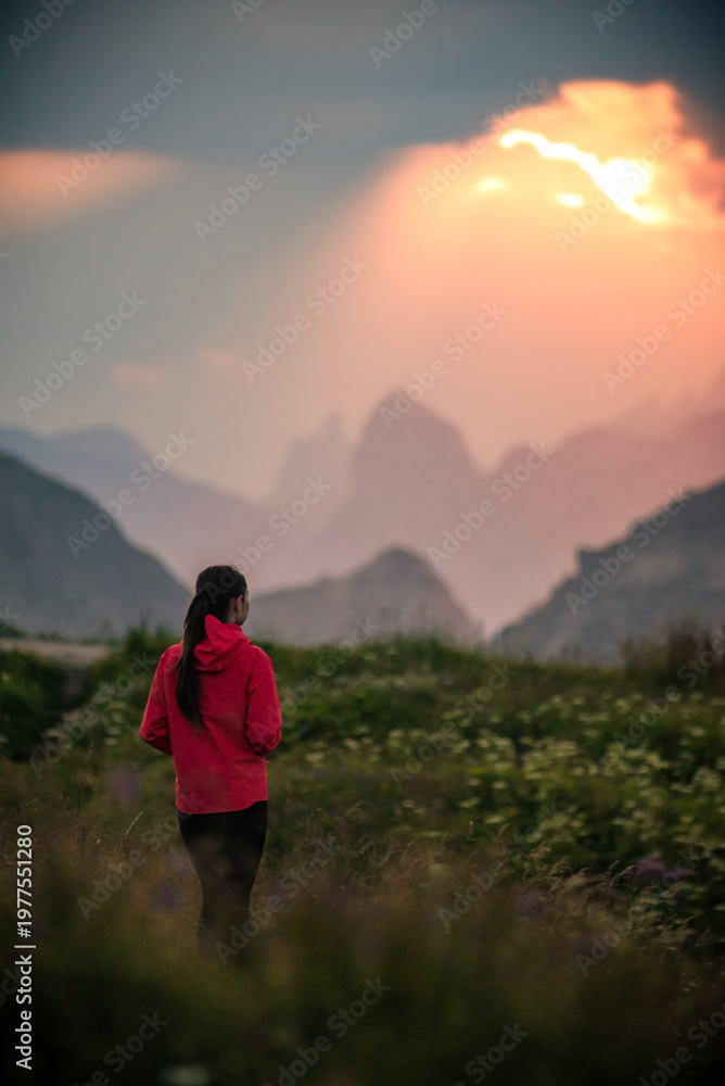 Fototapeta premium Girl in red jacket watching sunset over mountains