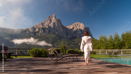 Woman in white robe walking to the infinity pool, enjoying luxury lifestyle on summer vacation at hotel spa with mountain view	