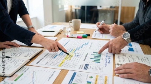 Close-up of team members pointing at charts and notes during a meeting, focus on hands and materials rather than faces, dynamic interaction suggesting planning and