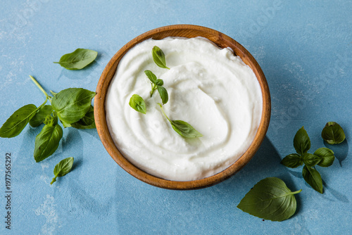 Obraz na płótnie Sour cream or greek yoghurt, in a bowl on a table with basil leaves