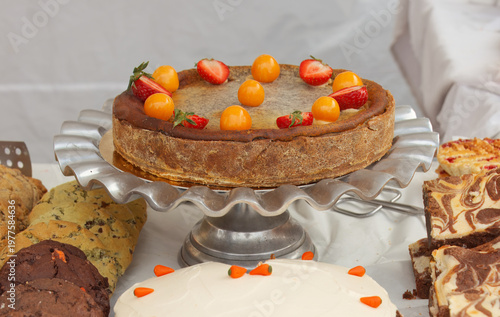Delicious artisanal cake topped with fresh strawberries and golden berries on a silver stand. Perfect for food blogs or showcasing sweet treats at Prague vibrant Naplavka farmers market.