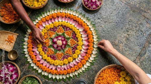 Top view of hands arranging a colorful flower mandala on a stone floor. Traditional floral rangoli decoration flat lay