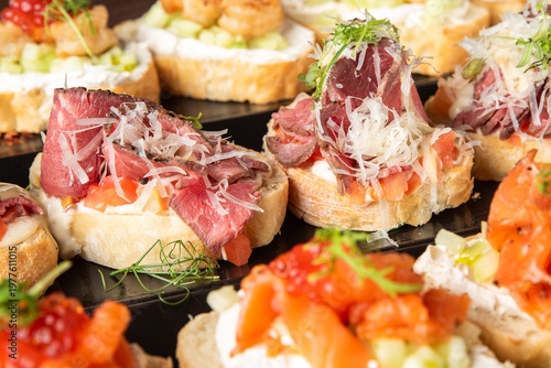 Assorted gourmet bruschetta appetizers with roast beef, smoked salmon, red caviar, and fresh microgreens on a black platter